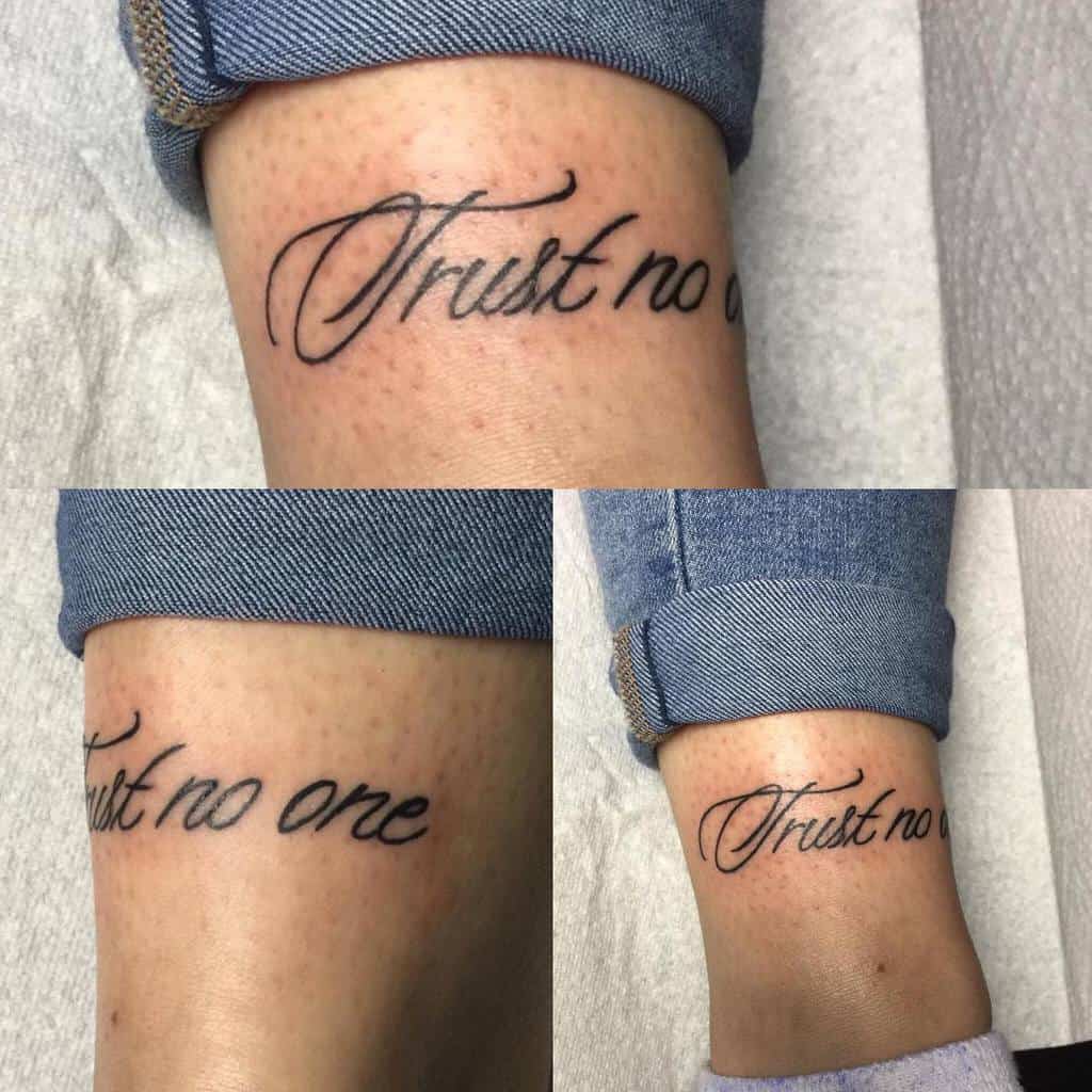 Tattoo on a person's ankle reading "Trust no one" in cursive font