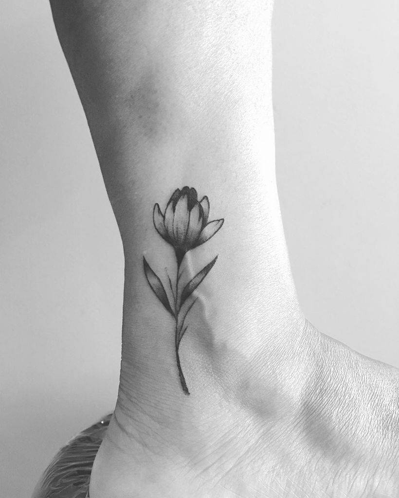 A delicate black and grey tulip tattoo on the ankle, featuring fine shading and a slender stem for an elegant and minimalist design.