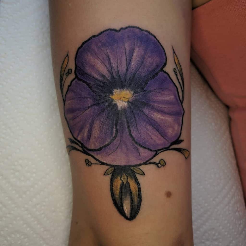 Bold tattoo of a vibrant purple pansy with intricate shading and golden ornamental details, symbolizing love, remembrance, and beauty