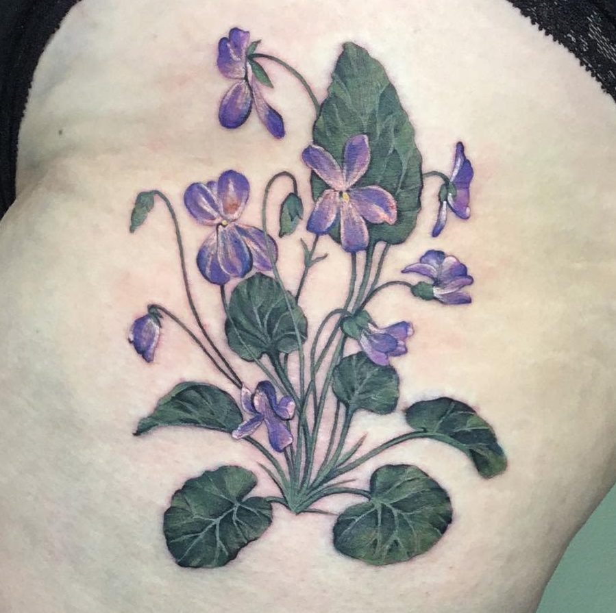 Realistic tattoo of a lush violet flower cluster with deep green leaves, symbolizing nature, resilience, and delicate beauty