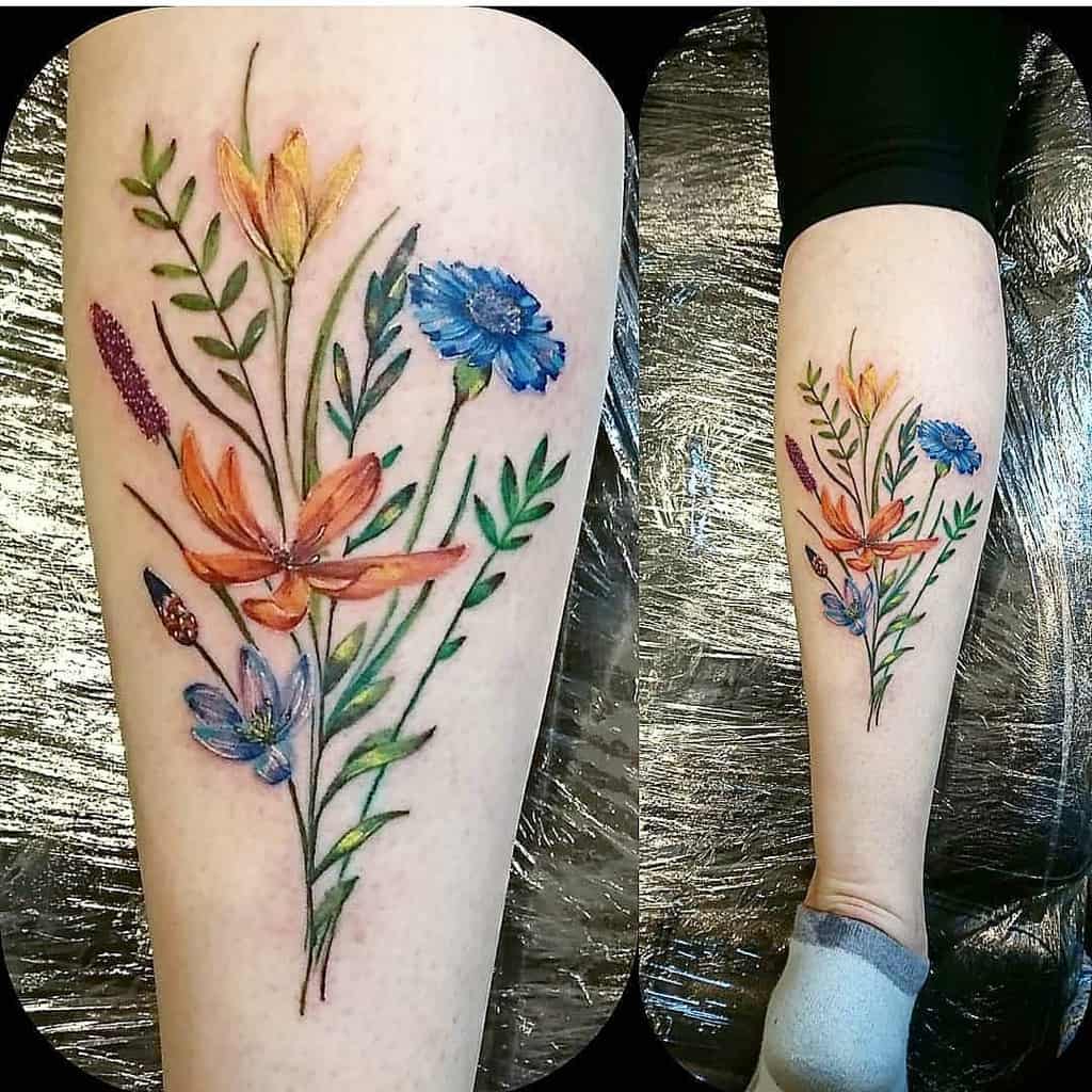 Colorful floral tattoo on a leg featuring leaves and various flowers