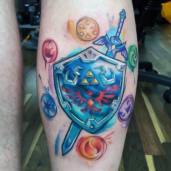 Vibrant leg tattoo of the Hylian Shield and Master Sword from The Legend of Zelda, surrounded by colorful elemental symbols in a watercolor style.