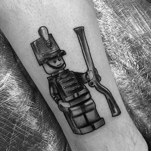 Black and grey tattoo of a Lego toy soldier holding a musket, featuring classic uniform details and smooth shading for depth.