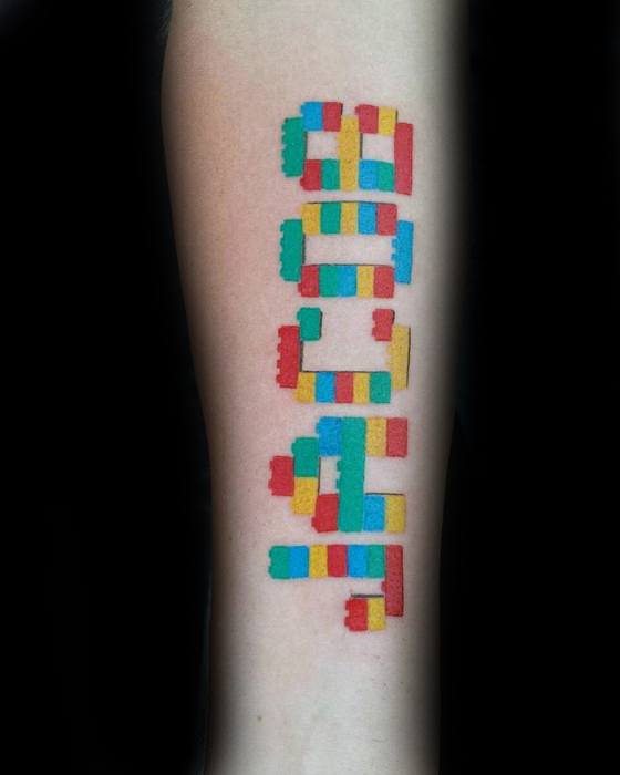 Colorful tattoo of Lego bricks arranged vertically to spell "BUILD" in red, yellow, blue, and green on the forearm.