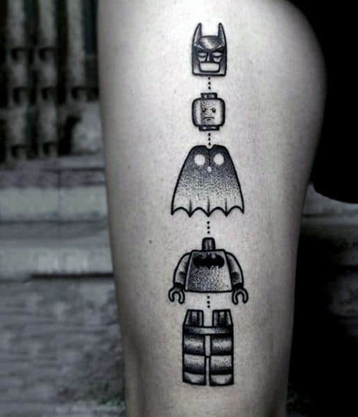 Dotwork tattoo of a deconstructed Lego Batman figure, with each body part stacked vertically and connected by a dashed line.