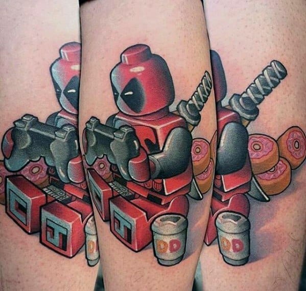 Colorful tattoo of Lego Deadpool playing video games, surrounded by donuts, coffee cups, and katanas in a fun, comic-style design.