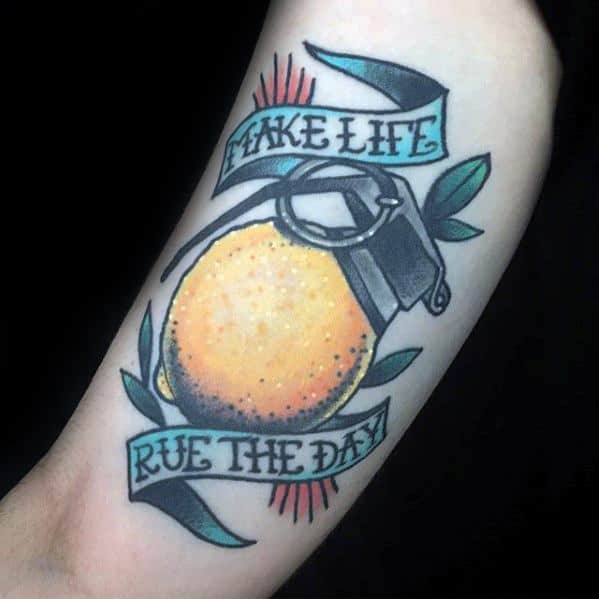 Tattoo of a lemon styled as a grenade, wrapped in banners reading "TAKE LIFE" and "RUE THE DAY," with bold colors and sharp outlines.