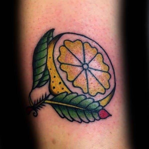 Traditional-style tattoo of a lemon slice wrapped in green leaves with bold outlines and vibrant yellow, green, and red coloring.