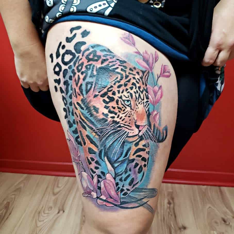 A colorful and detailed tattoo of a jaguar, surrounded by vibrant flowers and soft watercolor effects, placed on the thigh for a dynamic and artistic design.