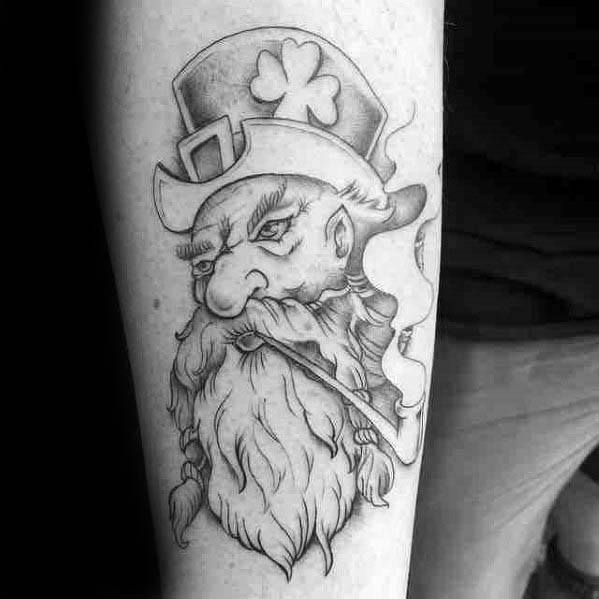 Black and grey leprechaun tattoo with a long beard, tilted hat with shamrock, and smoking a pipe with curling smoke.