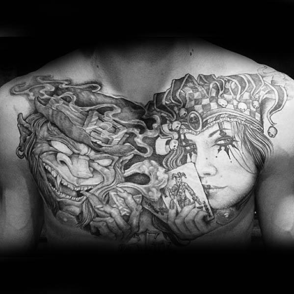 Detailed black and grey chest tattoo of a sinister leprechaun with swirling smoke beside a female jester holding a joker playing card.