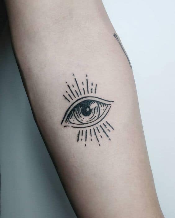 Minimalist black ink tattoo of an all-seeing eye with radiating lines, placed on the forearm.