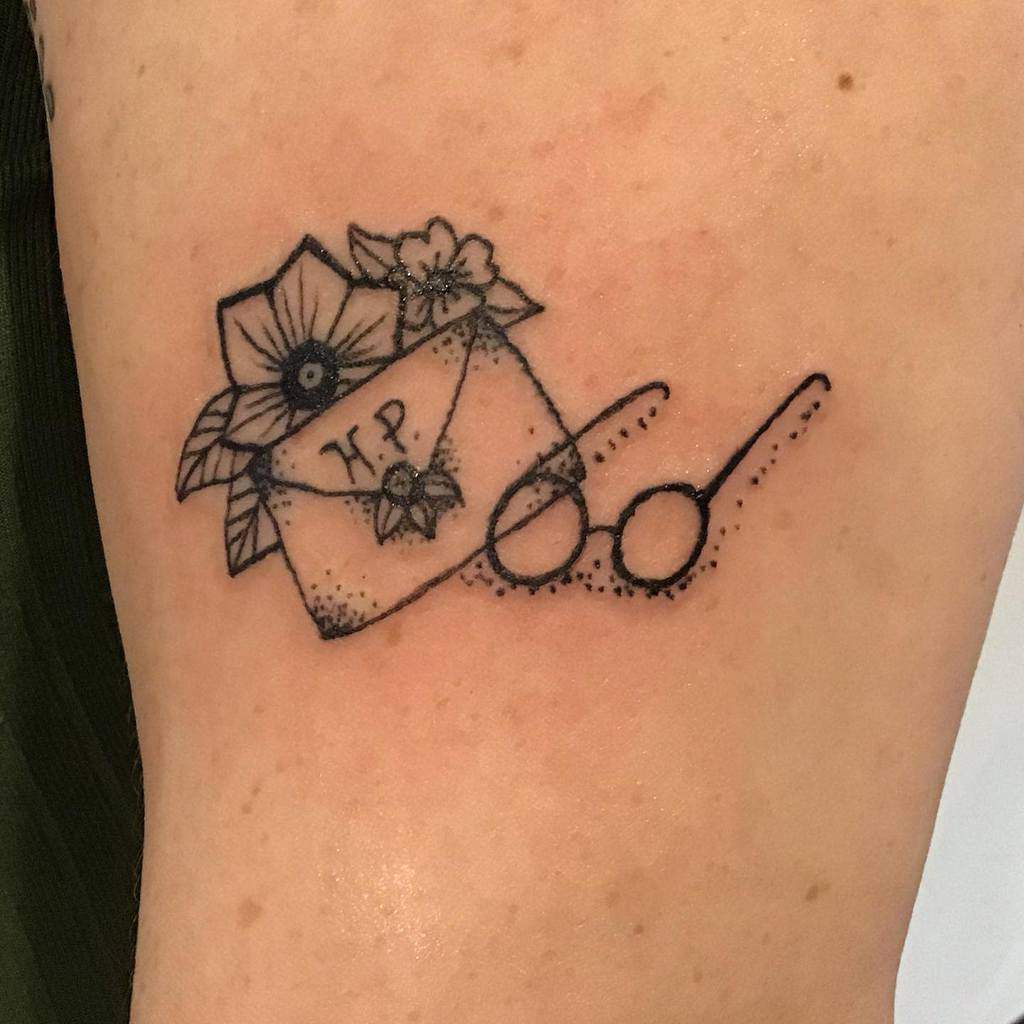 Minimalist Harry Potter tattoo featuring the iconic glasses, a Hogwarts acceptance letter with 'HP' initials, and floral details.