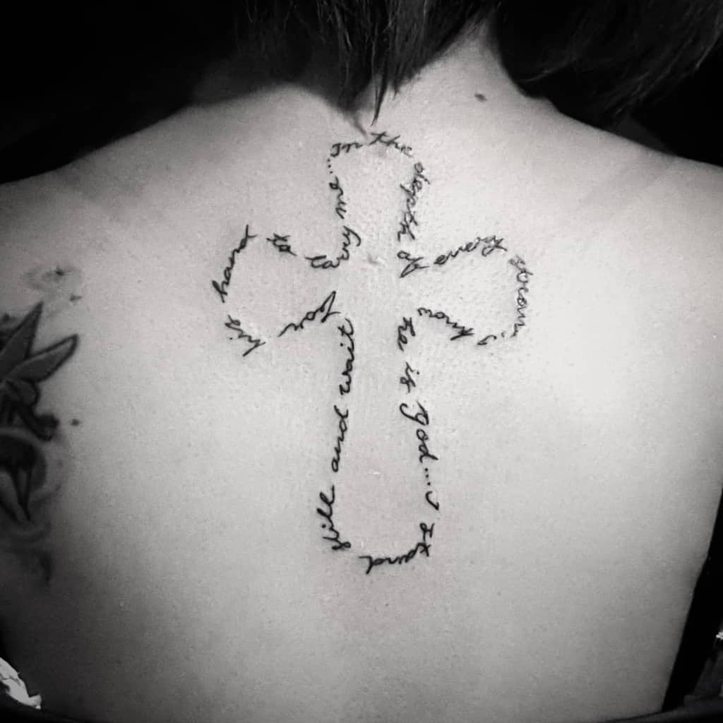 Tattoo of a cross elegantly woven with script text, gracing an upper back