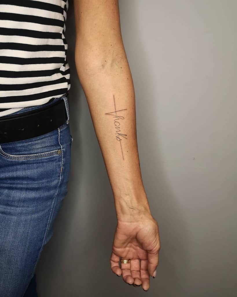 Forearm tattoo with cursive text "thanks" and a subtle cross