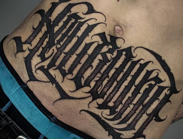 Blackwork tattoo across the stomach featuring bold, gothic-style lettering with intricate details and sharp, dramatic edges.