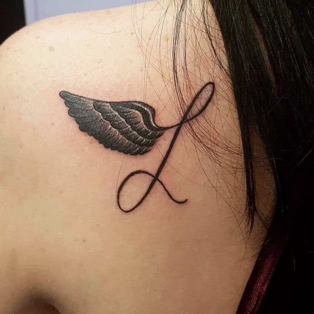 Close-up of a tattoo featuring a detailed angel wing paired with an elegant, flowing 'L' letter