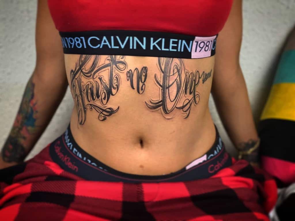 A person with "Trust No Love" tattooed on their abdomen