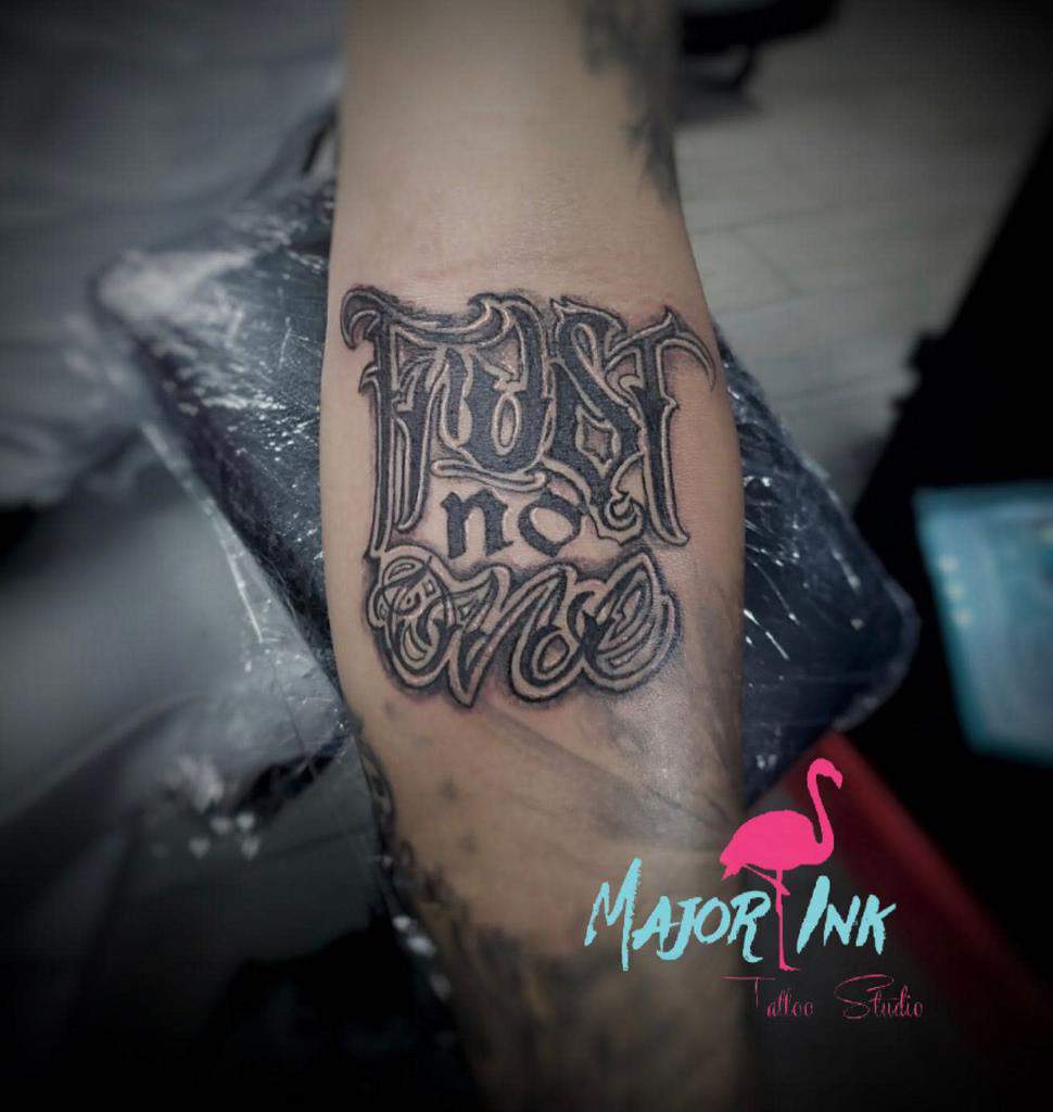 Tattoo on an arm reading "Trust no one" with stylized lettering