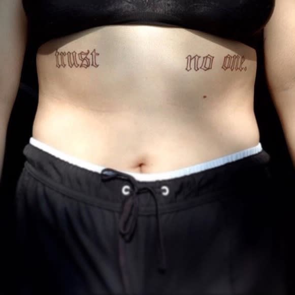 Person with "trust no one" tattooed on their ribs