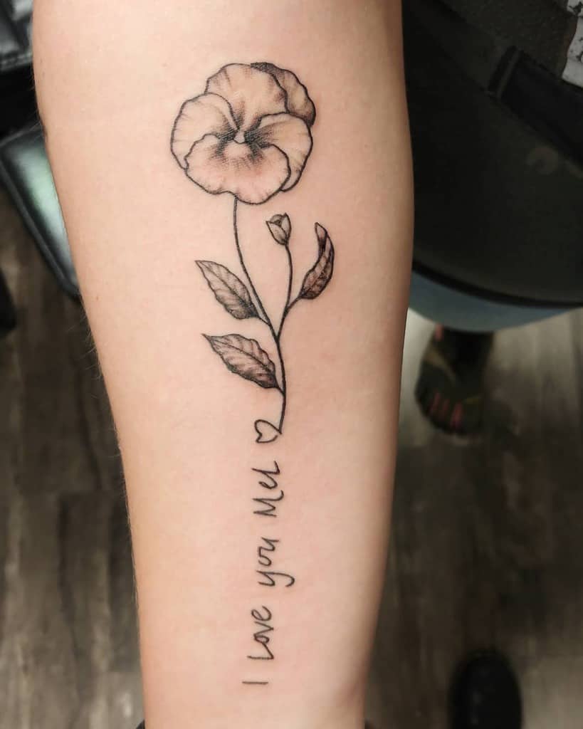 Delicate fine-line tattoo of a violet flower with leaves and a heartfelt handwritten message, 'I love you Mel,' symbolizing love and remembrance