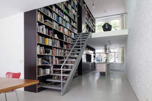 Modern loft with floor-to-ceiling library wall, sleek staircase, and minimalist kitchen design.