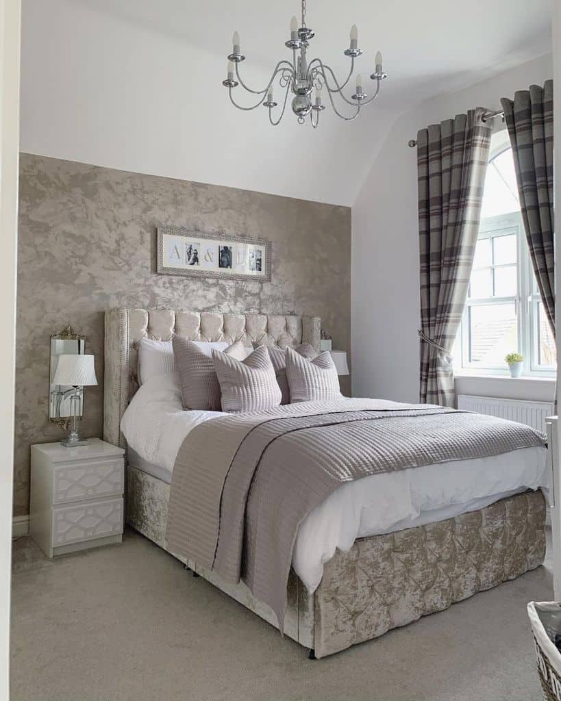 Elegant bedroom with a plush bed, gray bedding, chandelier, plaid curtains, and decorative framed photos on the wall