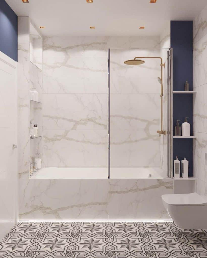 White marble bathroom with walk-in shower, gold fixtures, and patterned tile floor.