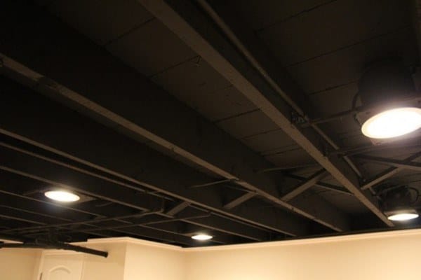 Basement with dark exposed beams, recessed spotlights, and modern industrial lighting fixtures.