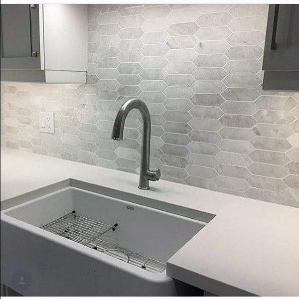 Light gray geometric tile backsplash with farmhouse sink and stainless steel faucet.