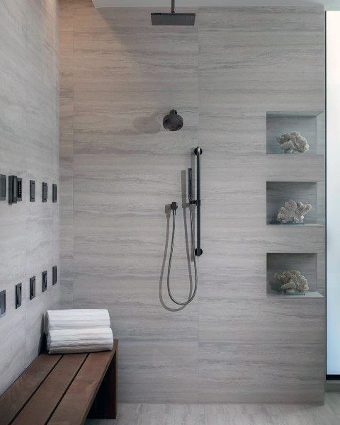 Travertine tile shower with built-in niches, rainfall showerhead, and wooden bench.