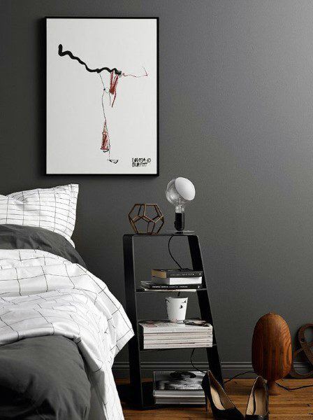 Bedroom with a grey wall, abstract art, bedside table, lamp, books, a coffee cup, shoes on wooden floor