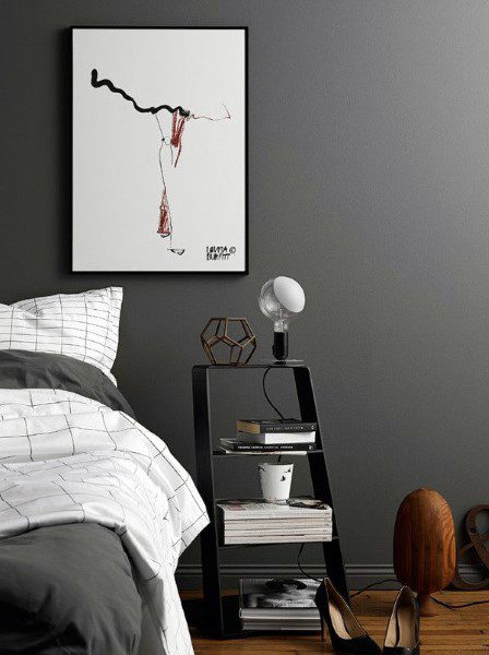 Minimalist grey bedroom with a bed, side table holding a lamp, books, and a coffee cup, and abstract art on the wall