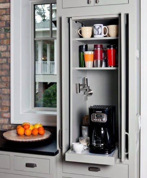 Compact coffee bar with light grey cabinets, pull-out shelf, coffee maker, and mugs.