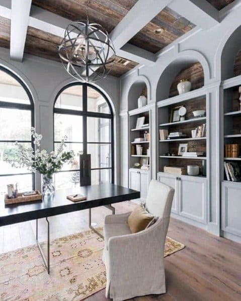 Home office with coffered wood ceiling, arched bookshelves, large windows, and modern desk.