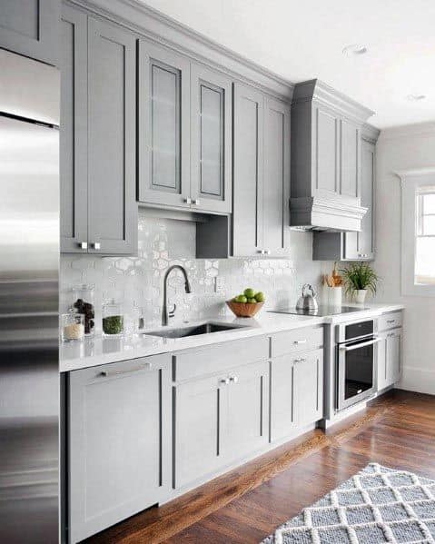 Light grey kitchen cabinets with white backsplash, stainless steel appliances, and hardwood flooring.