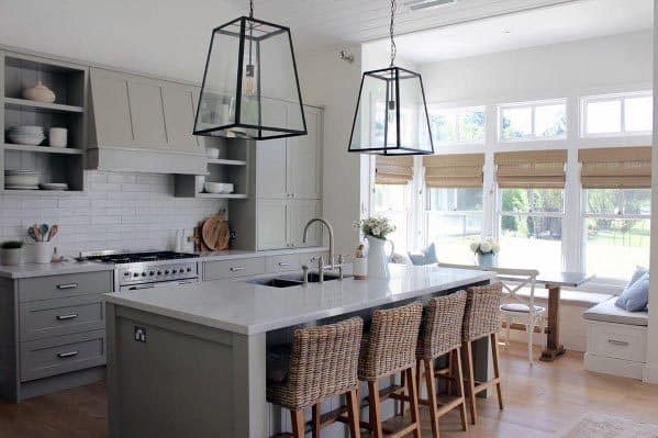 Light grey kitchen with wicker bar stools, white countertops, and large glass pendant lights.