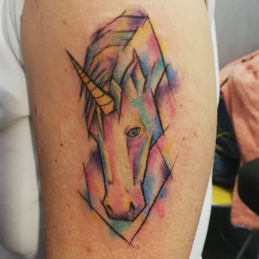 Watercolor-style unicorn tattoo with abstract splashes of blue, pink, and yellow, featuring fine black outlines for a dreamy artistic effect.