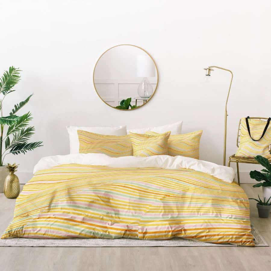 Yellow striped bed, round mirror, potted plants, and standing lamp fill this bright, airy bedroom