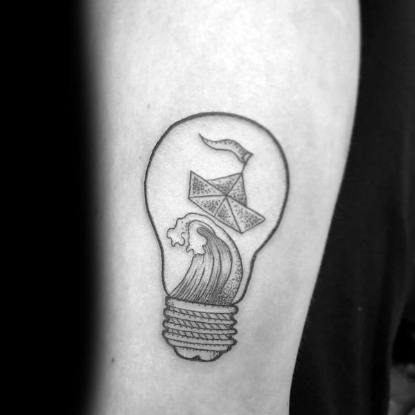 Paper boat and waves inside a light bulb tattoo, symbolizing creativity, adventure, and the power of imagination.