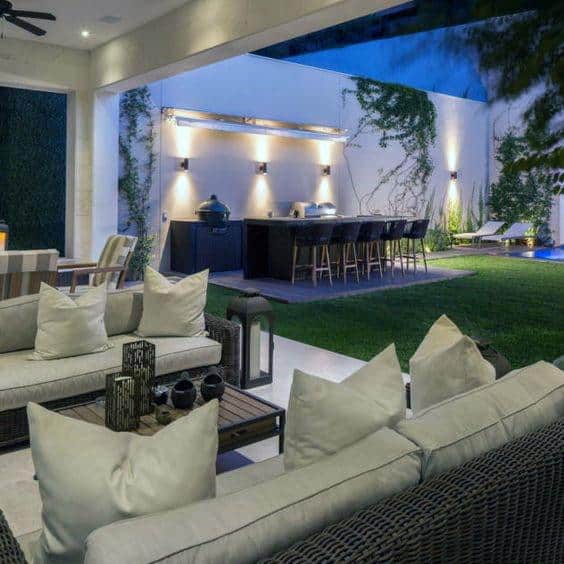 Modern outdoor kitchen bar with sleek lighting, barstools, and a cozy lounge area in a spacious backyard.