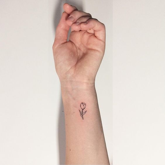 A small, delicate tulip tattoo on the wrist, featuring a fine-line black ink design with a simple flower and tiny leaves.