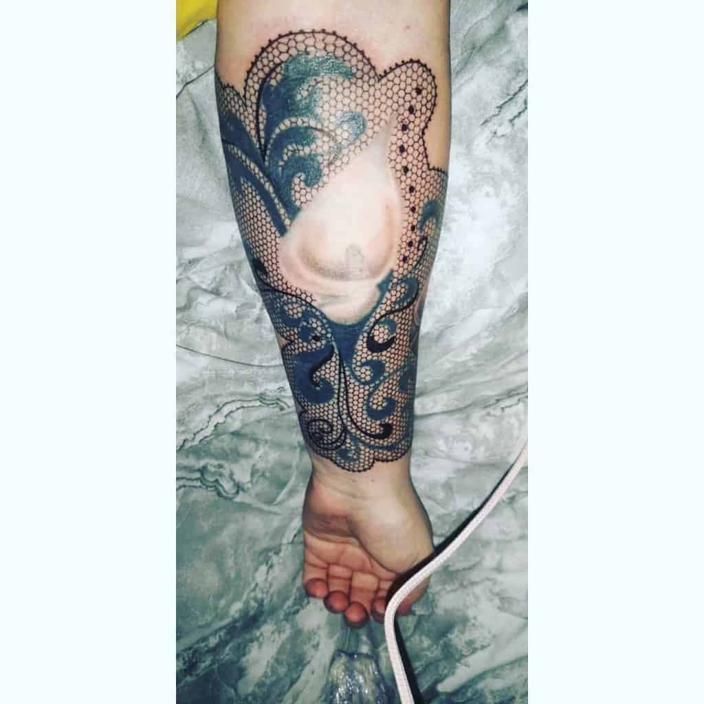 Unique forearm tattoo featuring intricate black lace patterns and ornamental swirls, framing a negative space design for a bold contrast.