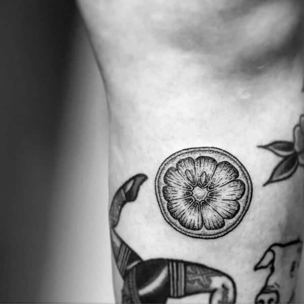 Fine line black ink lime slice tattoo with intricate shading, creating a delicate and detailed citrus-inspired design.