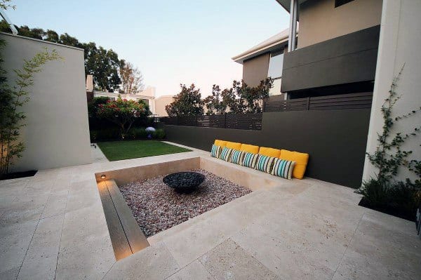 Modern backyard with limestone tiles, pebble fire pit, and yellow-striped seating.