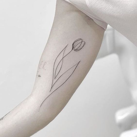 A minimalist black-line tulip tattoo on the upper arm, featuring an elegant flower with flowing lines and two smooth leaves.