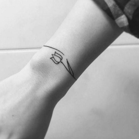 A minimalist black-line tulip tattoo on the wrist, featuring a simple geometric design with clean, angular lines.