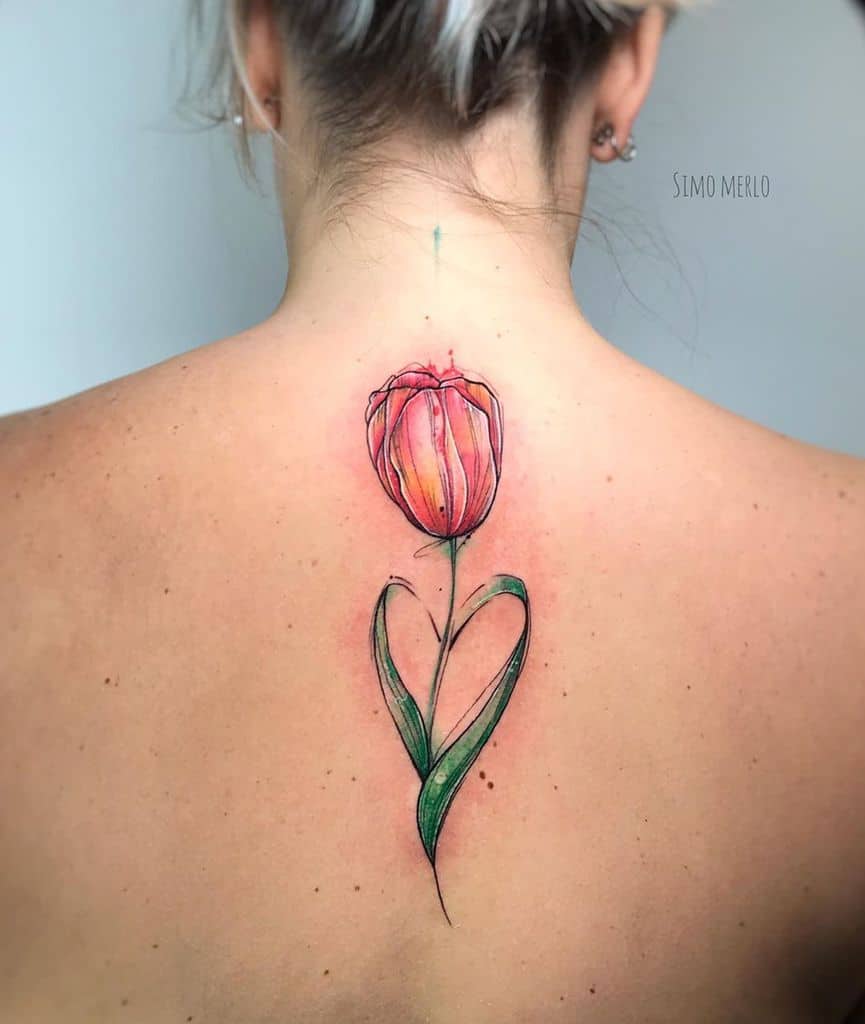 A vibrant watercolor tulip tattoo on the upper back, featuring a red and orange flower with green leaves forming a heart shape for a symbolic design.