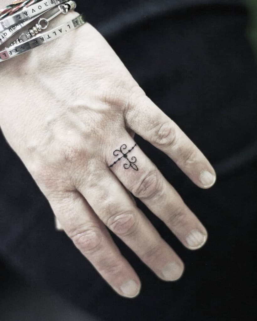 A minimalist ring tattoo featuring a small decorative swirling lines and dots, forming an elegant design