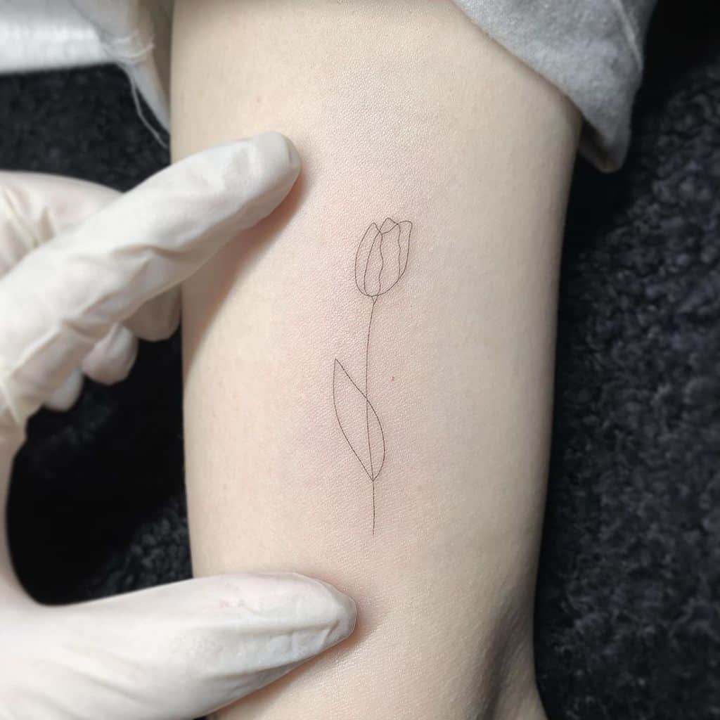 A delicate black-line tulip tattoo on the forearm, featuring a simple flower and a slender stem with a single leaf.